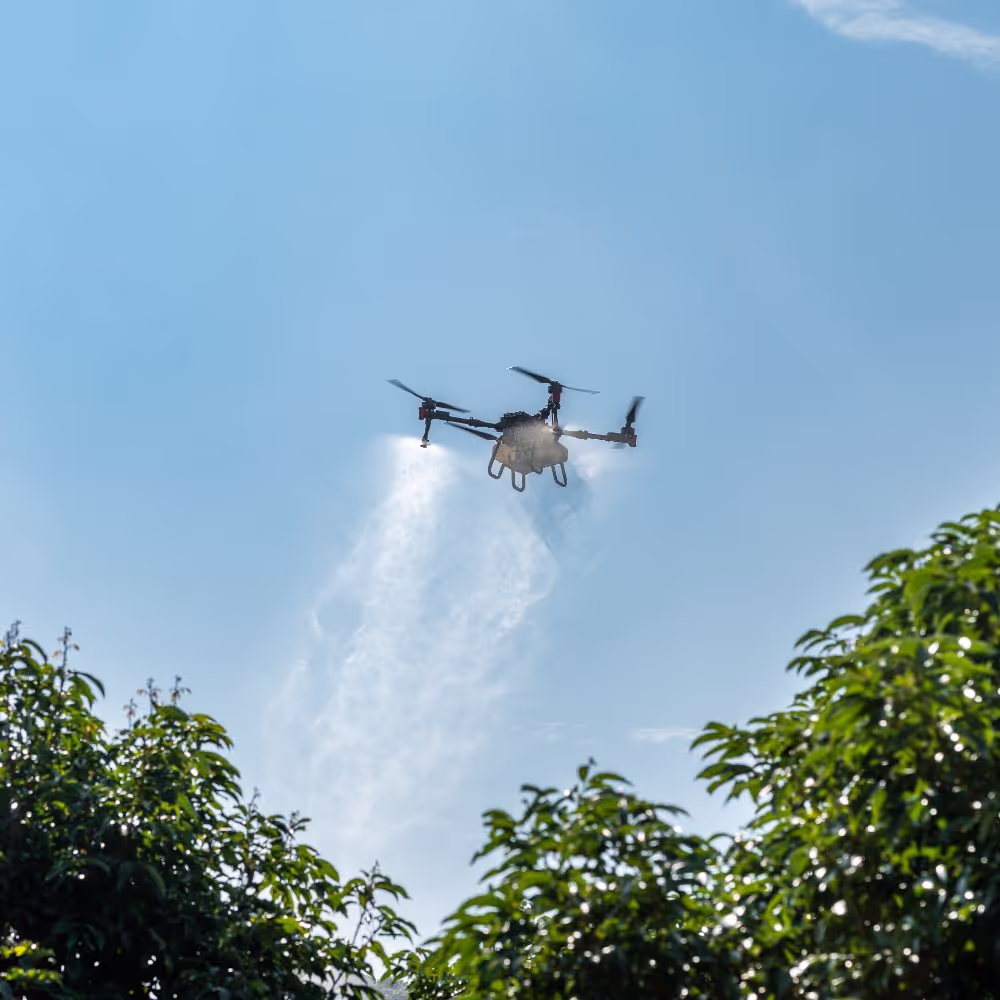 Agricultural drone spraying mist over crops with blue sky in the background.