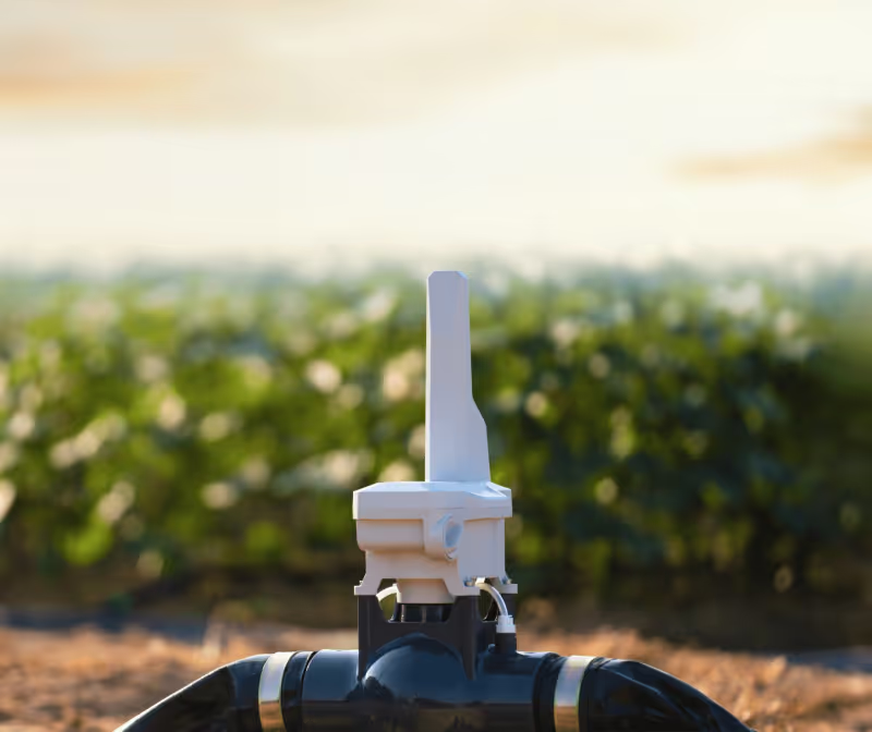 Close-up of a smart irrigation valve installed in farmland with green crops in the background.