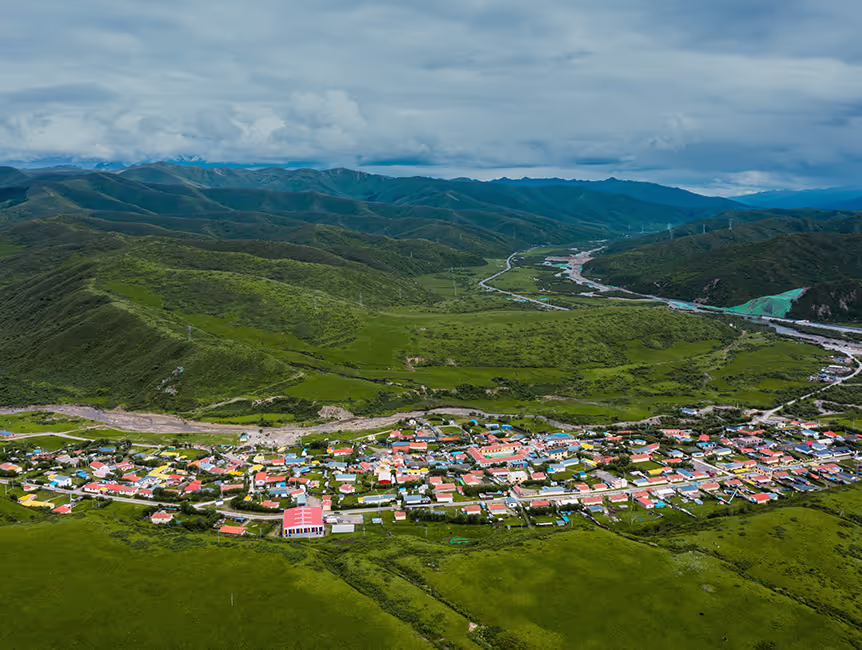 Aerial view of a small town with colorful roofs surrounded by green hills and a cloudy sky.